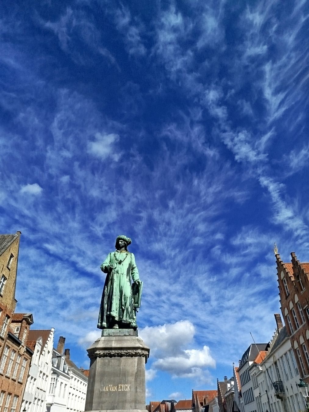 Van Eycmargolariaren estatua Bruggeko portuan, zeru dramatikoarekin.
