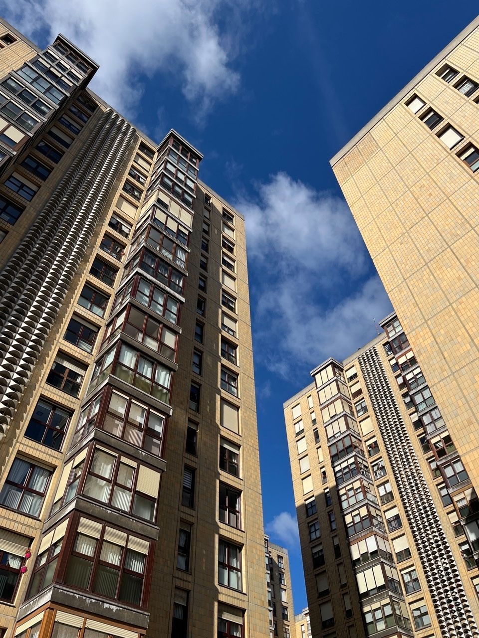 Etxebizitza-dorre batzuen argazkia. Eraikinak marroi argiak dira, eta zerua urdin dago hodei apur batzuekin. Argazkia behetik gora egin da.