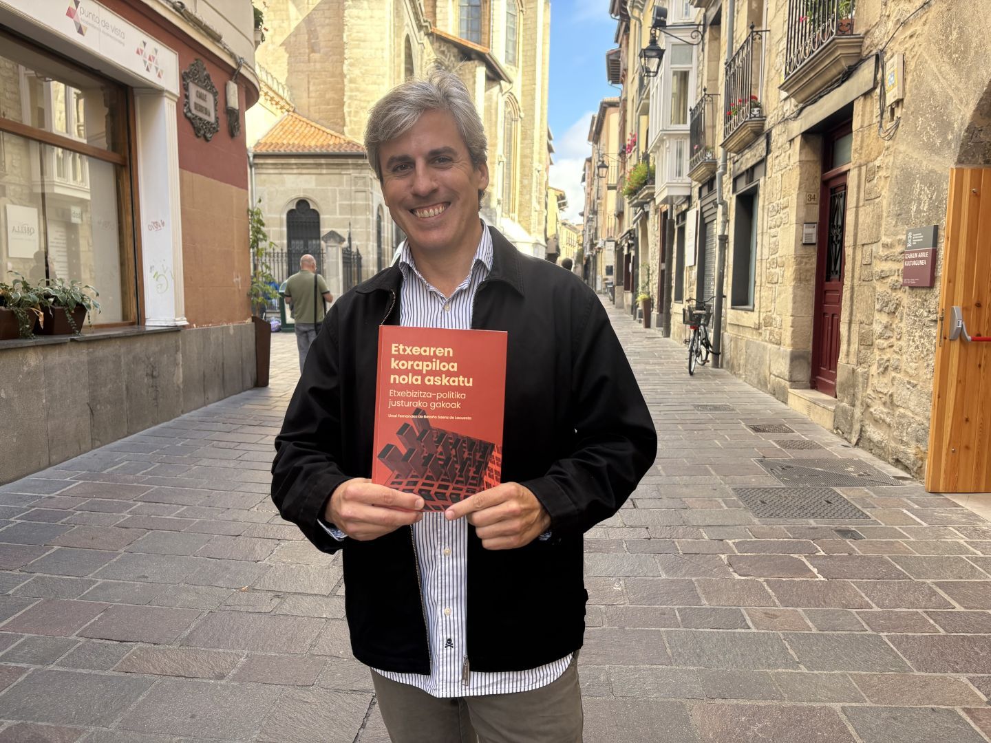 Unai Fernandez de Betoño Saenz de Lacuesta arkitekto doktorea ageri da "Etxearen korapiloa nola askatu. Etxebizitza-politika justurako gakoak " liburua eskuan duela, Gasteizko Alde Zaharrean